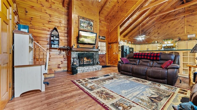 living room with beam ceiling, ceiling fan, wood walls, wood ceiling, and light wood-type flooring