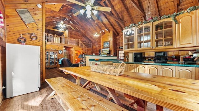 dining room featuring wood walls, ceiling fan, light hardwood / wood-style floors, beam ceiling, and wood ceiling