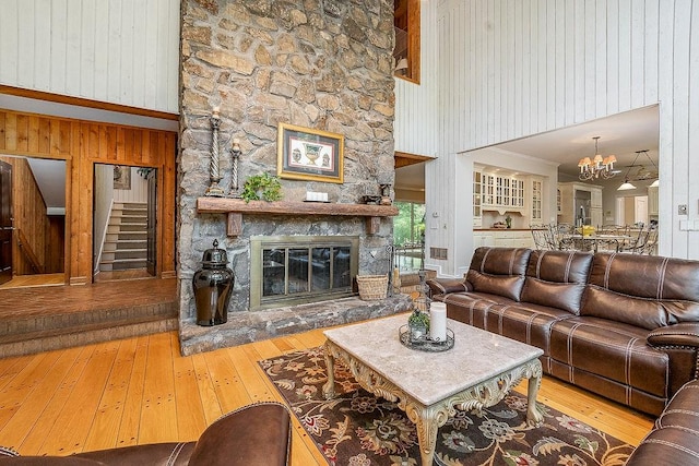 living room featuring a notable chandelier, hardwood / wood-style flooring, wooden walls, a stone fireplace, and a towering ceiling