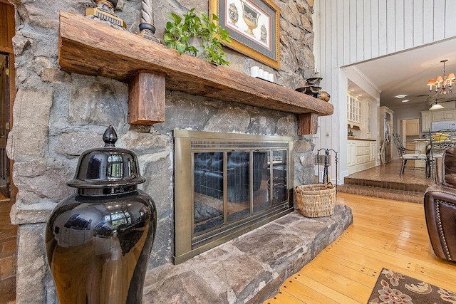 living room with a stone fireplace, hardwood / wood-style floors, a chandelier, and ornamental molding