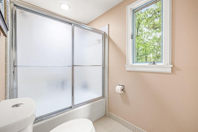 bathroom featuring shower / bath combination with glass door, toilet, tile patterned floors, and a healthy amount of sunlight