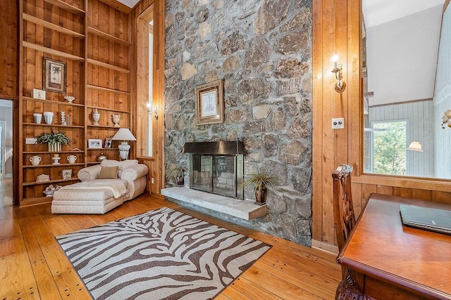 living room with built in features, lofted ceiling, a stone fireplace, and hardwood / wood-style floors