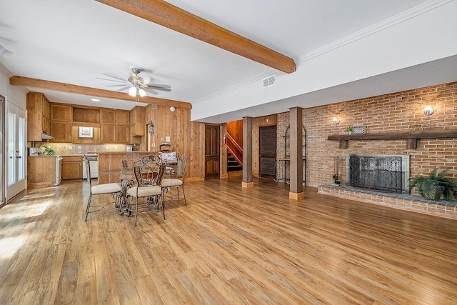 interior space with light hardwood / wood-style flooring, a fireplace, beam ceiling, brick wall, and ceiling fan