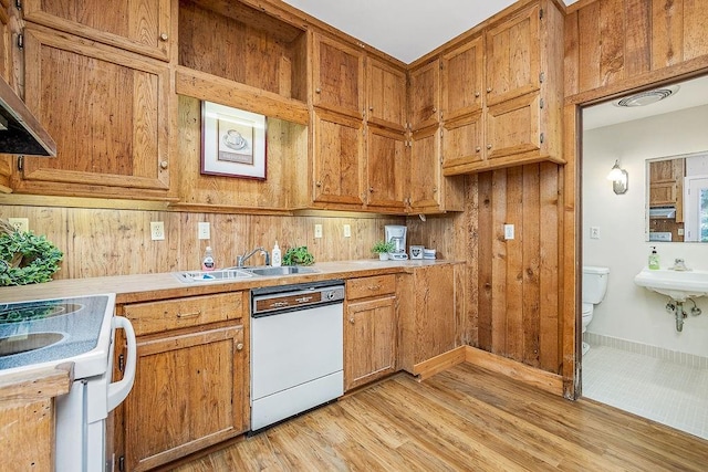 kitchen featuring light hardwood / wood-style flooring, wooden walls, white appliances, premium range hood, and sink