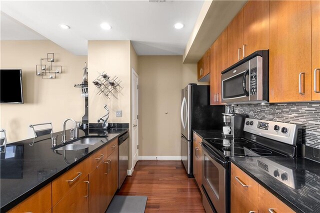 kitchen featuring appliances with stainless steel finishes, dark hardwood / wood-style flooring, tasteful backsplash, dark stone counters, and sink