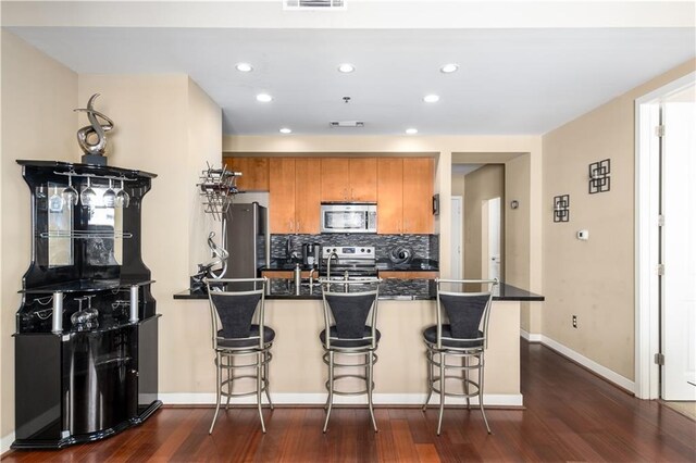 kitchen featuring a breakfast bar, kitchen peninsula, dark wood-type flooring, and appliances with stainless steel finishes