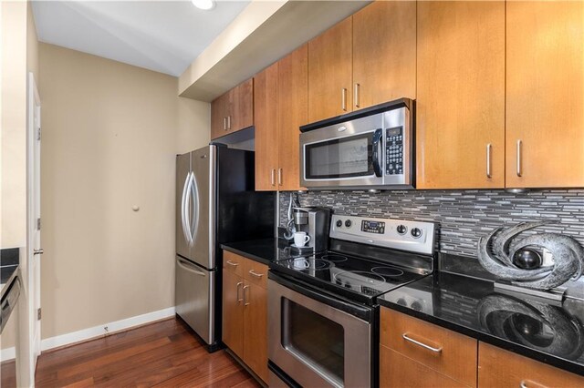 kitchen with appliances with stainless steel finishes, tasteful backsplash, dark wood-type flooring, and dark stone countertops