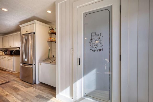 kitchen with washer and clothes dryer, white cabinets, stainless steel refrigerator, and light hardwood / wood-style floors