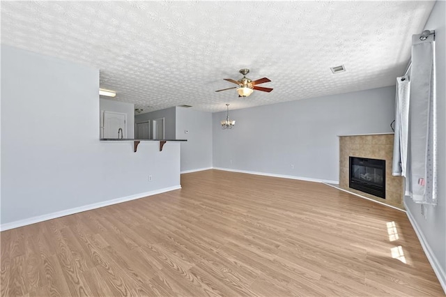 unfurnished living room featuring a fireplace, a textured ceiling, light hardwood / wood-style floors, and ceiling fan with notable chandelier