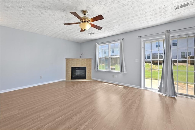 unfurnished living room with hardwood / wood-style floors, a textured ceiling, ceiling fan, and a tiled fireplace