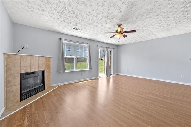 unfurnished living room with hardwood / wood-style flooring, ceiling fan, a textured ceiling, and a tiled fireplace