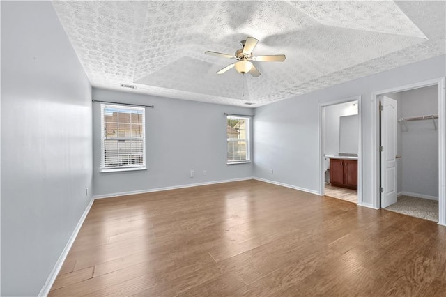 unfurnished bedroom featuring multiple windows, ensuite bathroom, ceiling fan, and light hardwood / wood-style floors