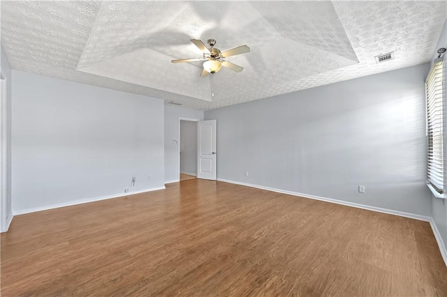 unfurnished room with a tray ceiling, ceiling fan, wood-type flooring, and a textured ceiling