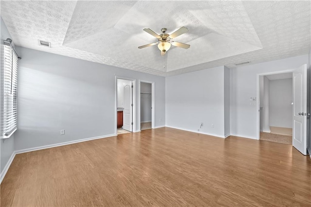 unfurnished bedroom featuring a walk in closet, ensuite bathroom, a tray ceiling, ceiling fan, and hardwood / wood-style flooring