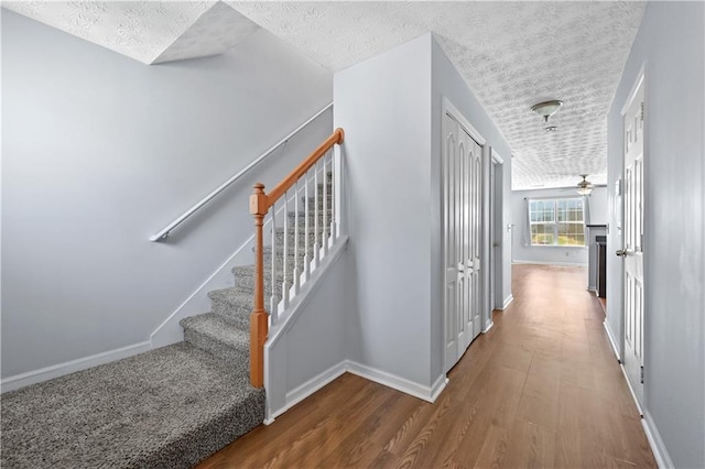 stairs featuring ceiling fan, wood-type flooring, and a textured ceiling