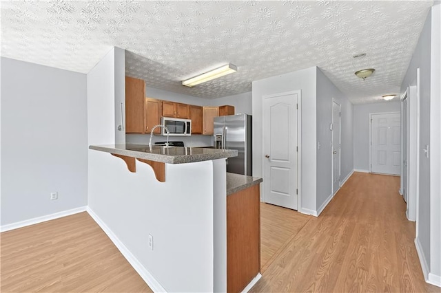 kitchen featuring kitchen peninsula, a textured ceiling, stainless steel appliances, and light hardwood / wood-style floors