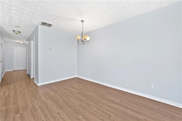 unfurnished room featuring wood-type flooring, a textured ceiling, and an inviting chandelier