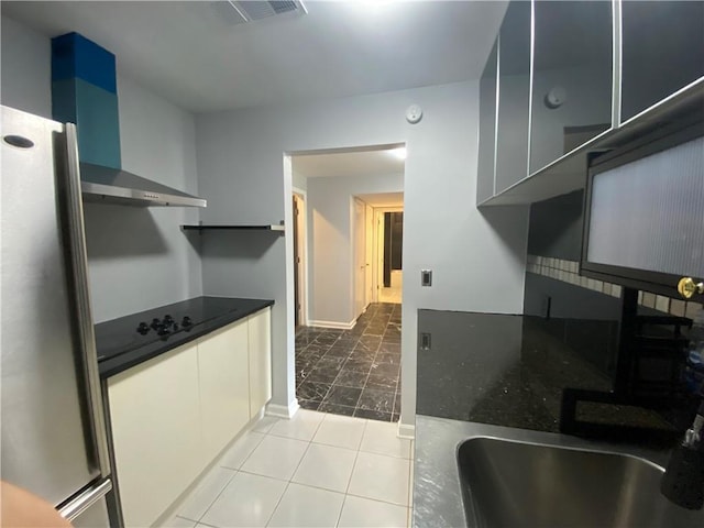 kitchen featuring wall chimney range hood, dark countertops, a sink, freestanding refrigerator, and visible vents