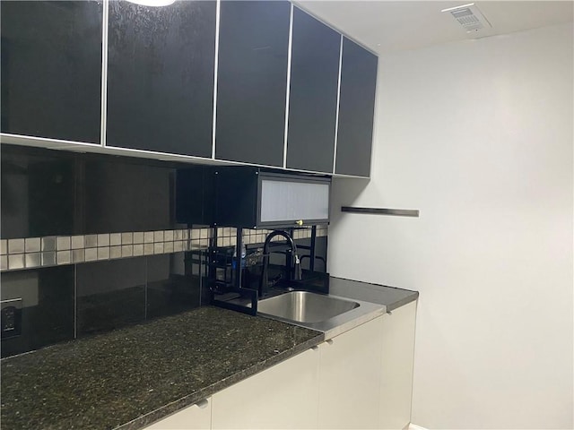 kitchen with visible vents, a sink, and dark stone counters