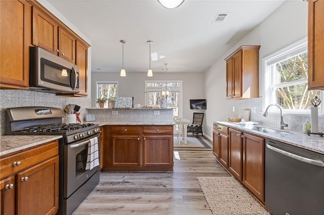 kitchen with visible vents, a peninsula, a sink, stainless steel appliances, and light wood-style floors