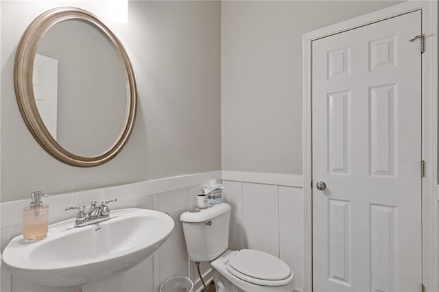 half bathroom with a sink, a wainscoted wall, and toilet