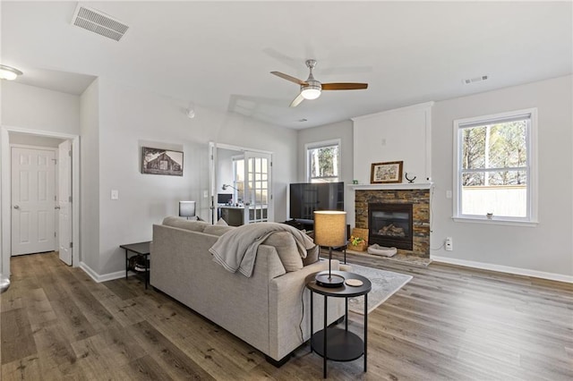 living room featuring visible vents, baseboards, a stone fireplace, and wood finished floors