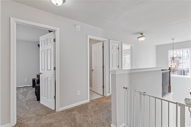 corridor featuring an inviting chandelier, carpet, and baseboards