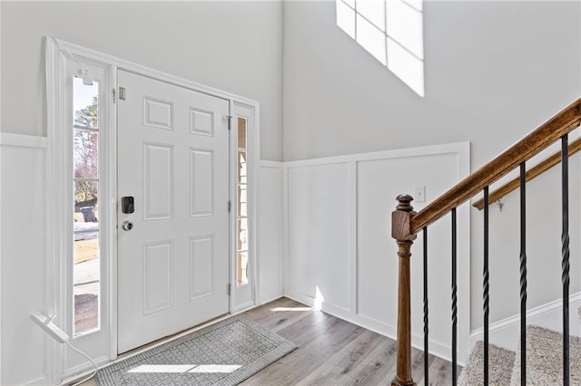 foyer entrance featuring stairway, a decorative wall, wood finished floors, and wainscoting