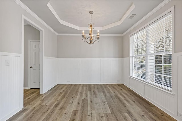 spare room with a chandelier, visible vents, a tray ceiling, and wood finished floors