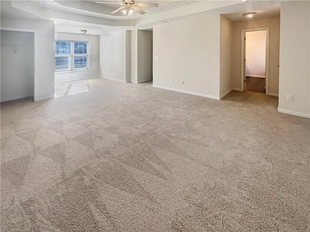 empty room with a tray ceiling, carpet, ceiling fan, and baseboards