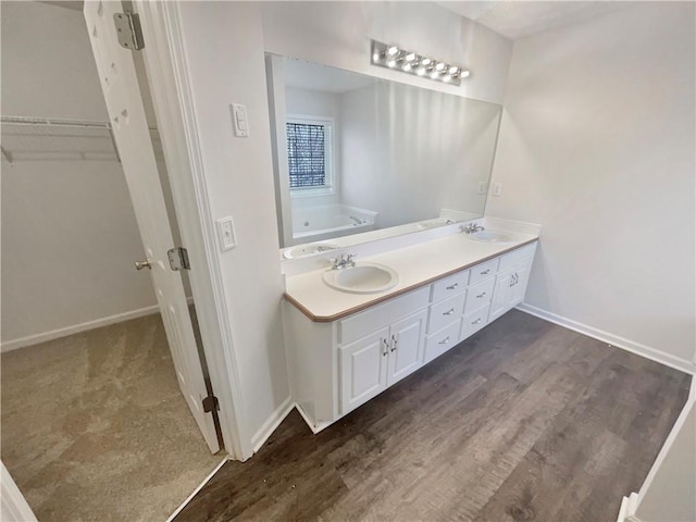 full bath featuring a walk in closet, a sink, baseboards, and double vanity