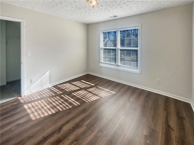 empty room featuring a textured ceiling, dark wood-style flooring, visible vents, and baseboards