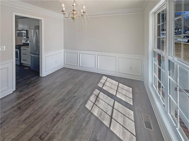 unfurnished dining area featuring dark wood-style floors, visible vents, a decorative wall, ornamental molding, and a chandelier