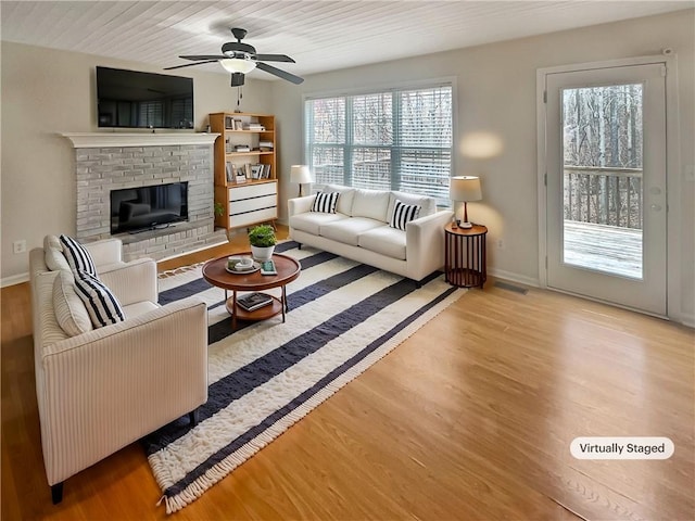 living area featuring ceiling fan, a brick fireplace, wood finished floors, and baseboards