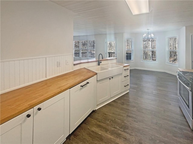 kitchen with stainless steel electric range oven, butcher block counters, dark wood-type flooring, an inviting chandelier, and a sink