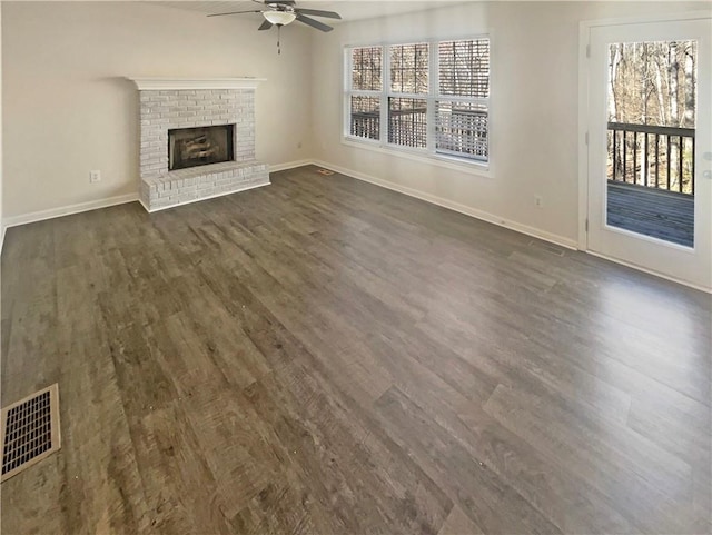 unfurnished living room with a brick fireplace, dark wood finished floors, visible vents, and baseboards