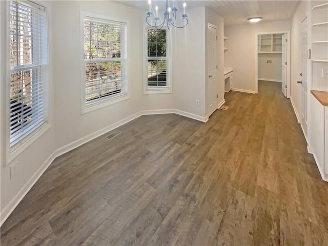 unfurnished dining area featuring baseboards, a notable chandelier, visible vents, and dark wood-style flooring