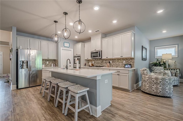 3715 Bridges Ct, Cumming, GA 30040 - kitchen with appliances with stainless steel finishes, an island with sink, light countertops, a sink, and tasteful backsplash