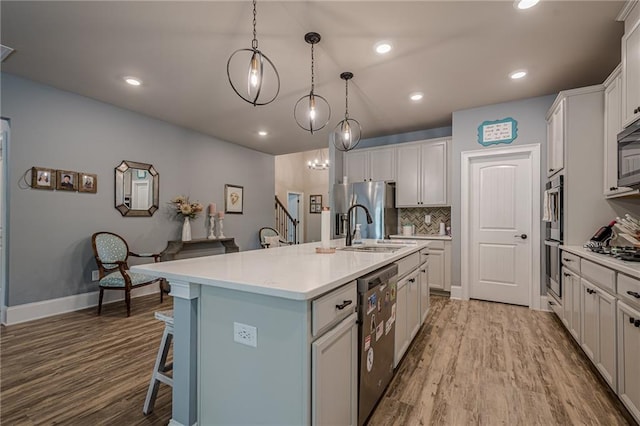 3715 Bridges Ct, Cumming, GA 30040 - kitchen featuring stainless steel appliances, wood finished floors, a sink, a kitchen island with sink, and a kitchen bar