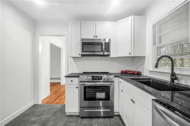 kitchen with appliances with stainless steel finishes, sink, dark stone counters, and white cabinets