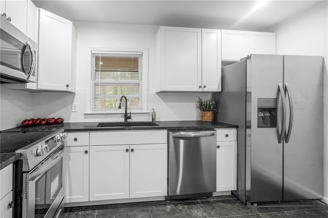 kitchen featuring appliances with stainless steel finishes, white cabinetry, sink, backsplash, and dark stone counters