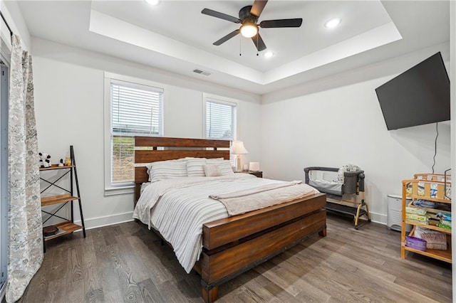 bedroom featuring visible vents, a tray ceiling, wood finished floors, recessed lighting, and baseboards