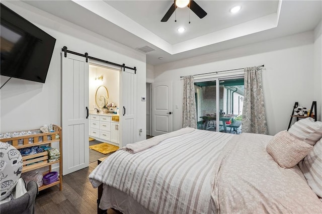 bedroom with visible vents, connected bathroom, a tray ceiling, a barn door, and dark wood-style flooring