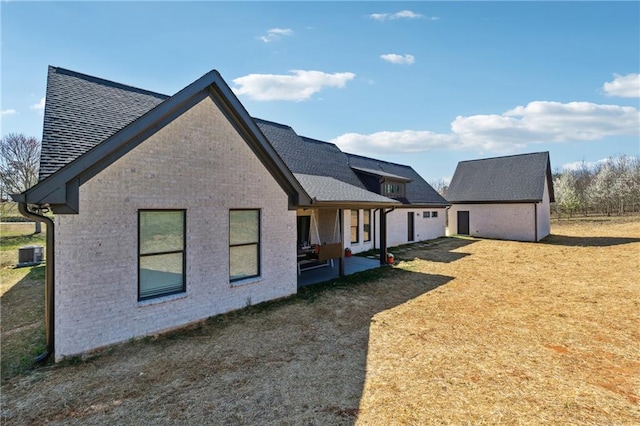 view of side of home with an outbuilding, a patio, central AC, a shingled roof, and brick siding