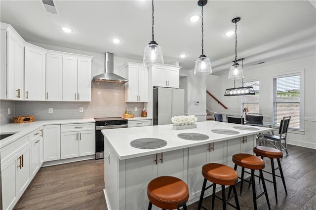 kitchen with a center island, appliances with stainless steel finishes, a breakfast bar area, wall chimney exhaust hood, and dark wood-style flooring