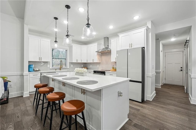 kitchen featuring a center island, white cabinets, freestanding refrigerator, and wall chimney range hood