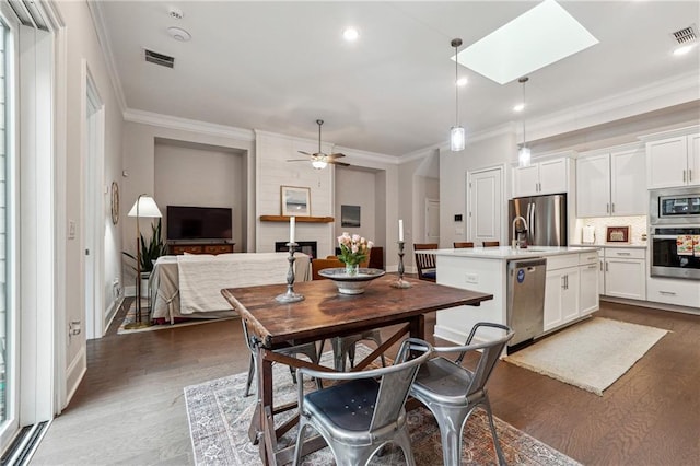 dining space featuring crown molding, a large fireplace, a skylight, and dark wood-type flooring