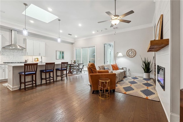 living room featuring dark hardwood / wood-style floors, a fireplace, a skylight, ornamental molding, and ceiling fan