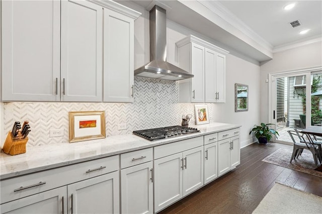 kitchen featuring wall chimney range hood, ornamental molding, stainless steel gas stovetop, light stone countertops, and white cabinets