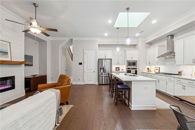 kitchen featuring a breakfast bar area, appliances with stainless steel finishes, white cabinetry, an island with sink, and wall chimney exhaust hood